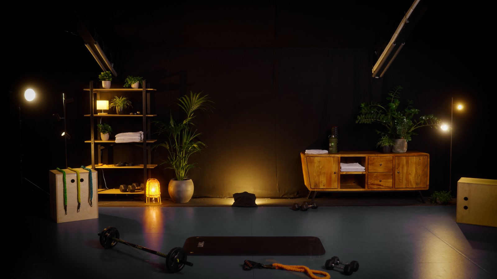 Ingerichte home-gym met dumbbells, weerstandsbanden, een houten kastje en warme spotlight-verlichting